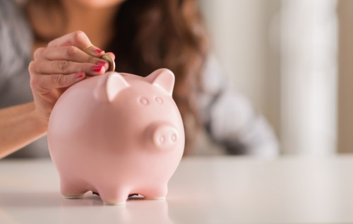 Woman Putting Coin In Piggy Bank, Indoors